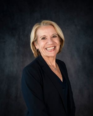 Professional headshot of someone in a black blazer smiling warmly against a dark background.