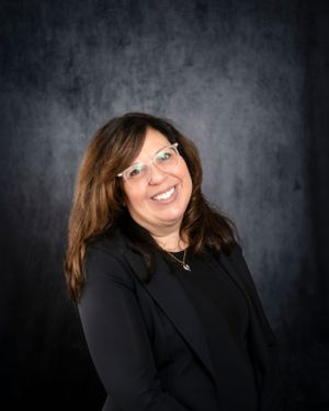Professional studio portrait of someone in a black top and glasses against a dark textured background.