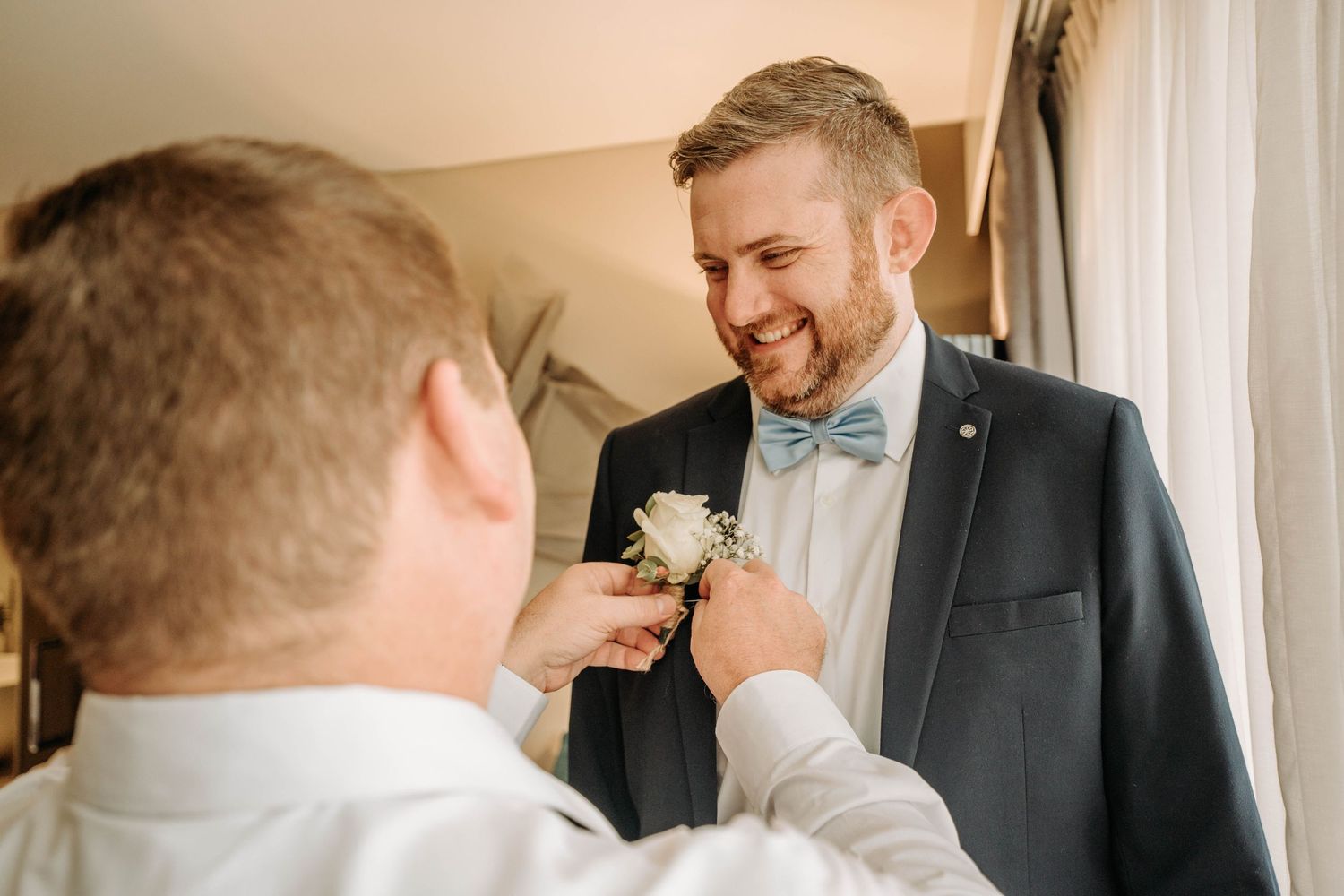 Groomsmen help each other with boutonnières while preparing for the wedding.