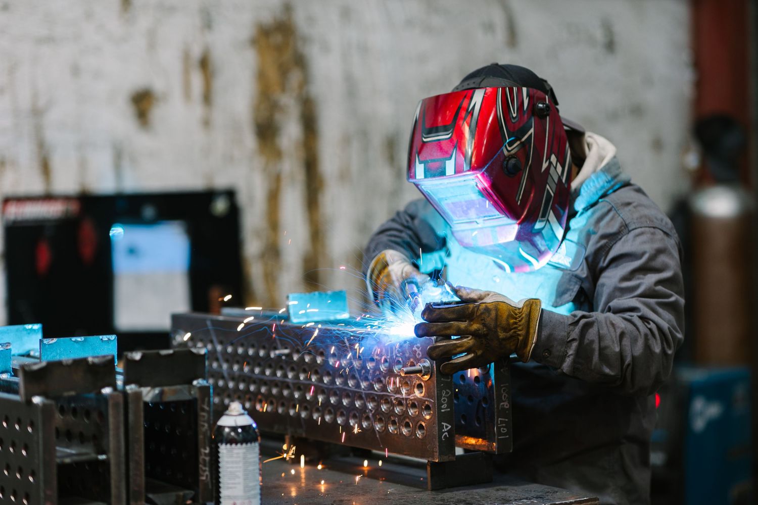 Welder wearing protective gear works on metal components in an industrial setting.