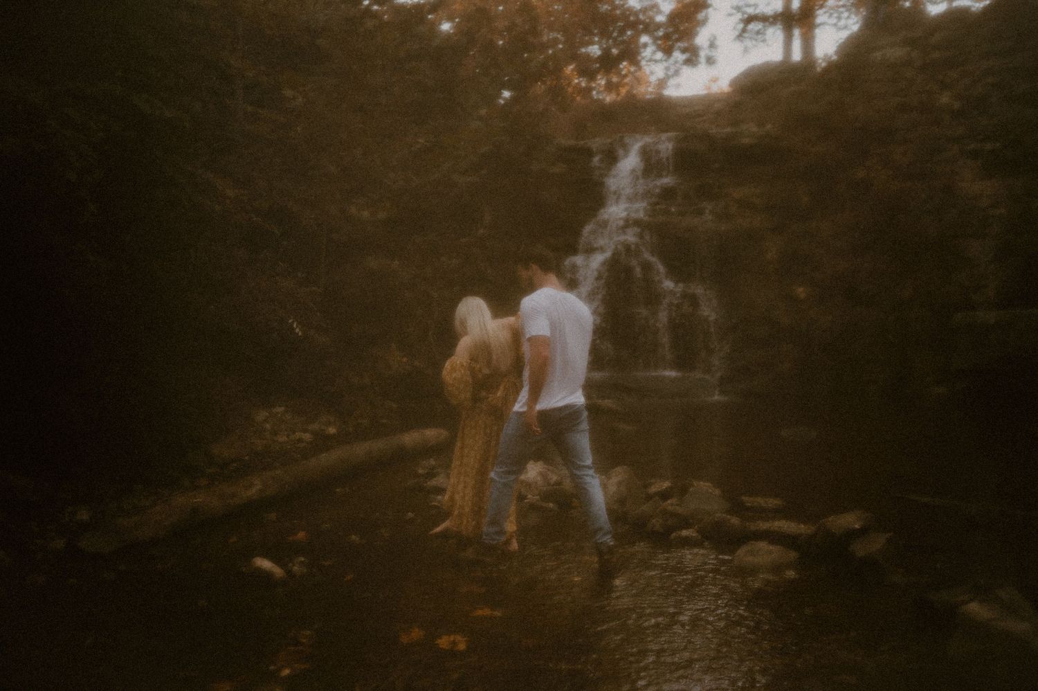 Indiana Couples Storytelling Photographer // Couple walking hand in hand through a waterfall at golden hour.