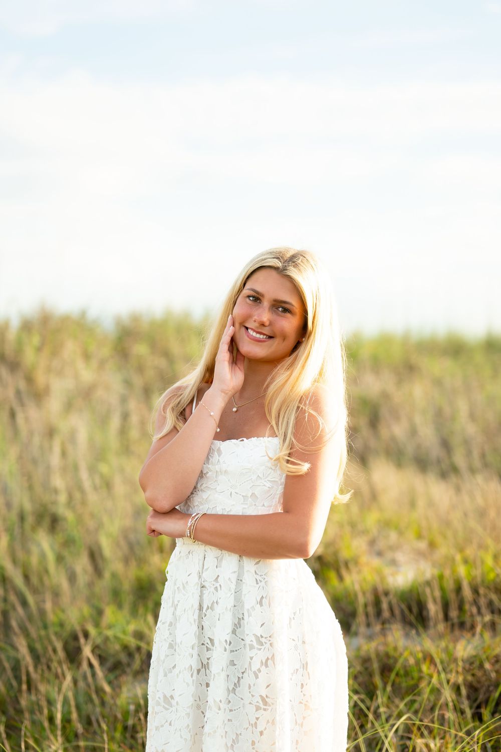 Woman in white lace dress poses joyfully in a sunlit meadow with golden grass.