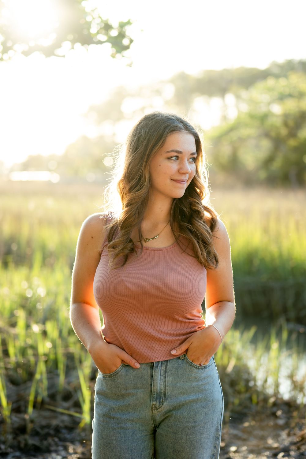 A golden sunset scene with a person in a pink top and jeans standing in tall grass.