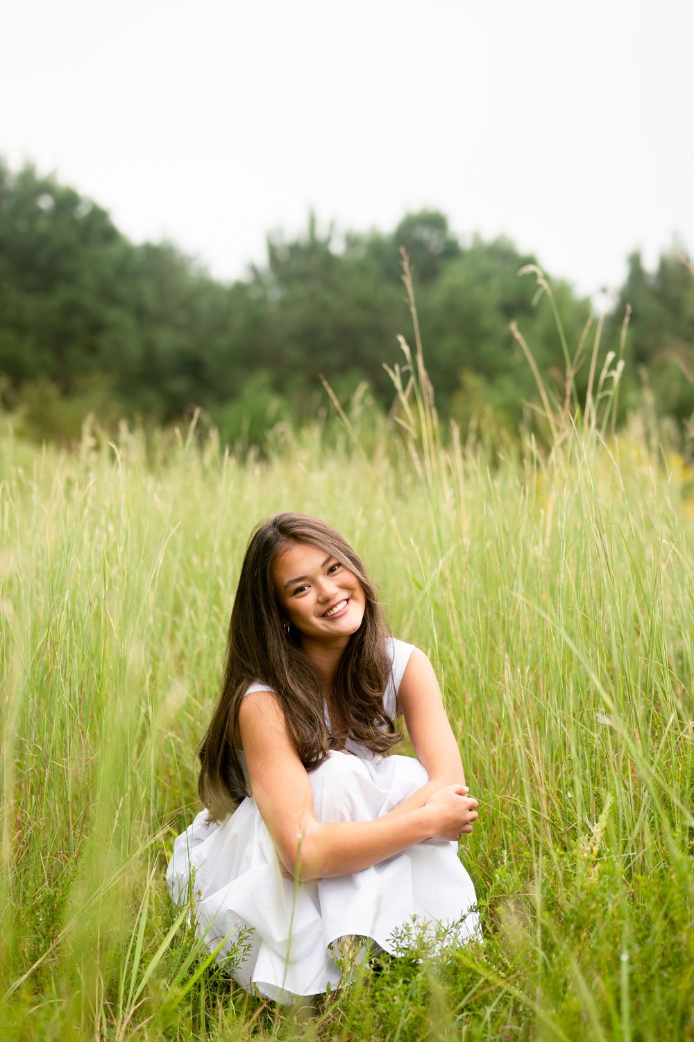 A person in a white dress lies joyfully in a sunlit meadow of tall grass during a summer day.