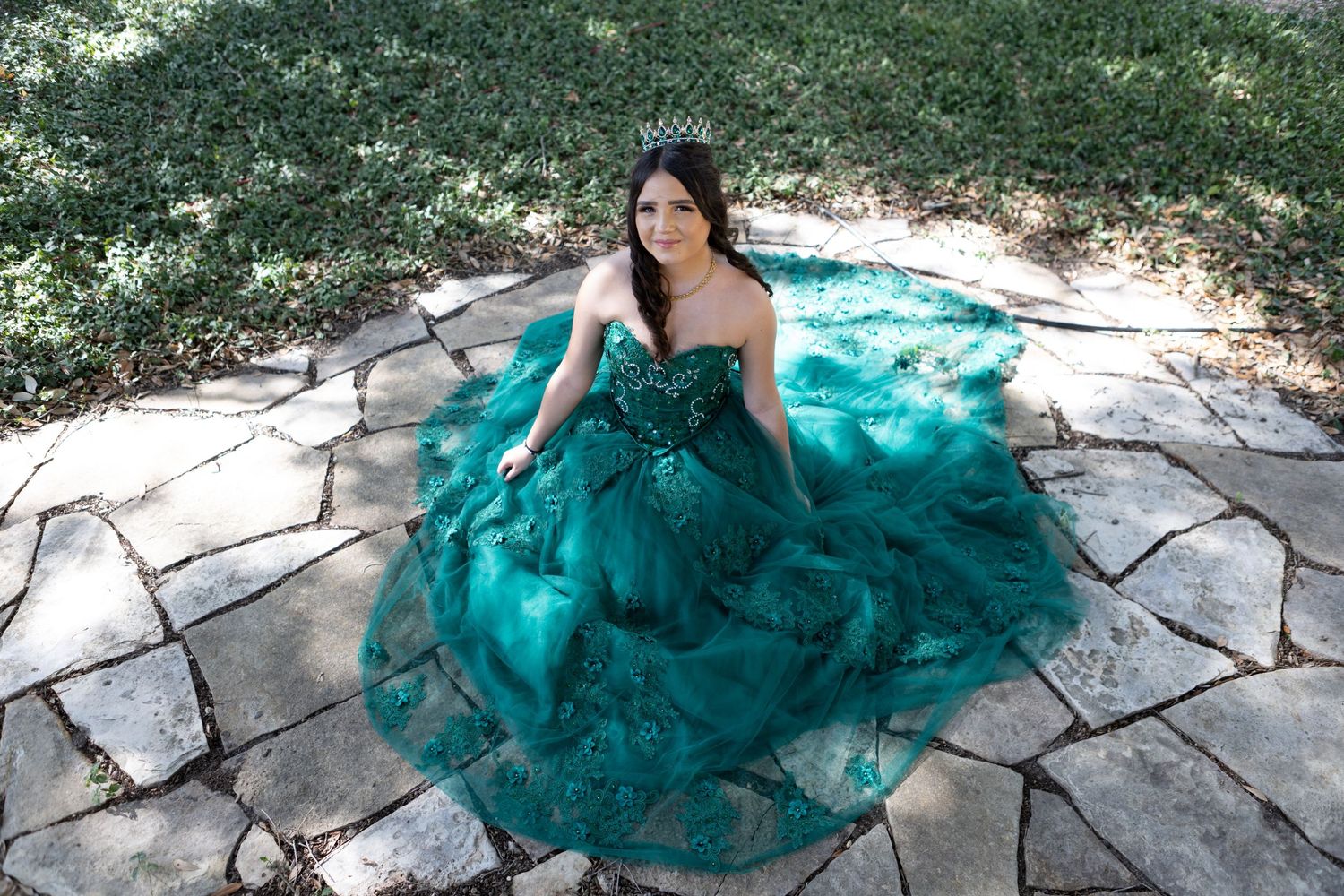 A person in a stunning teal ball gown sits on stone pavement in an outdoor setting.