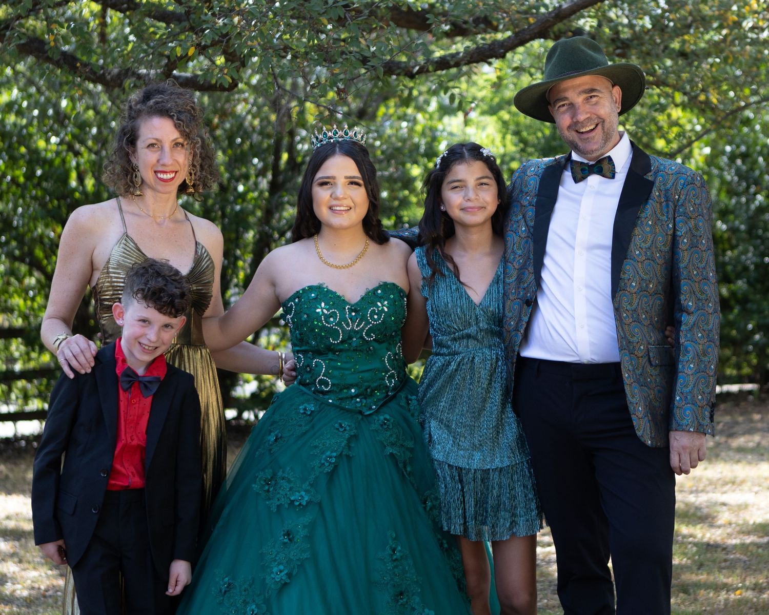 A group poses together outdoors, featuring formal attire and a distinctive teal ballgown.