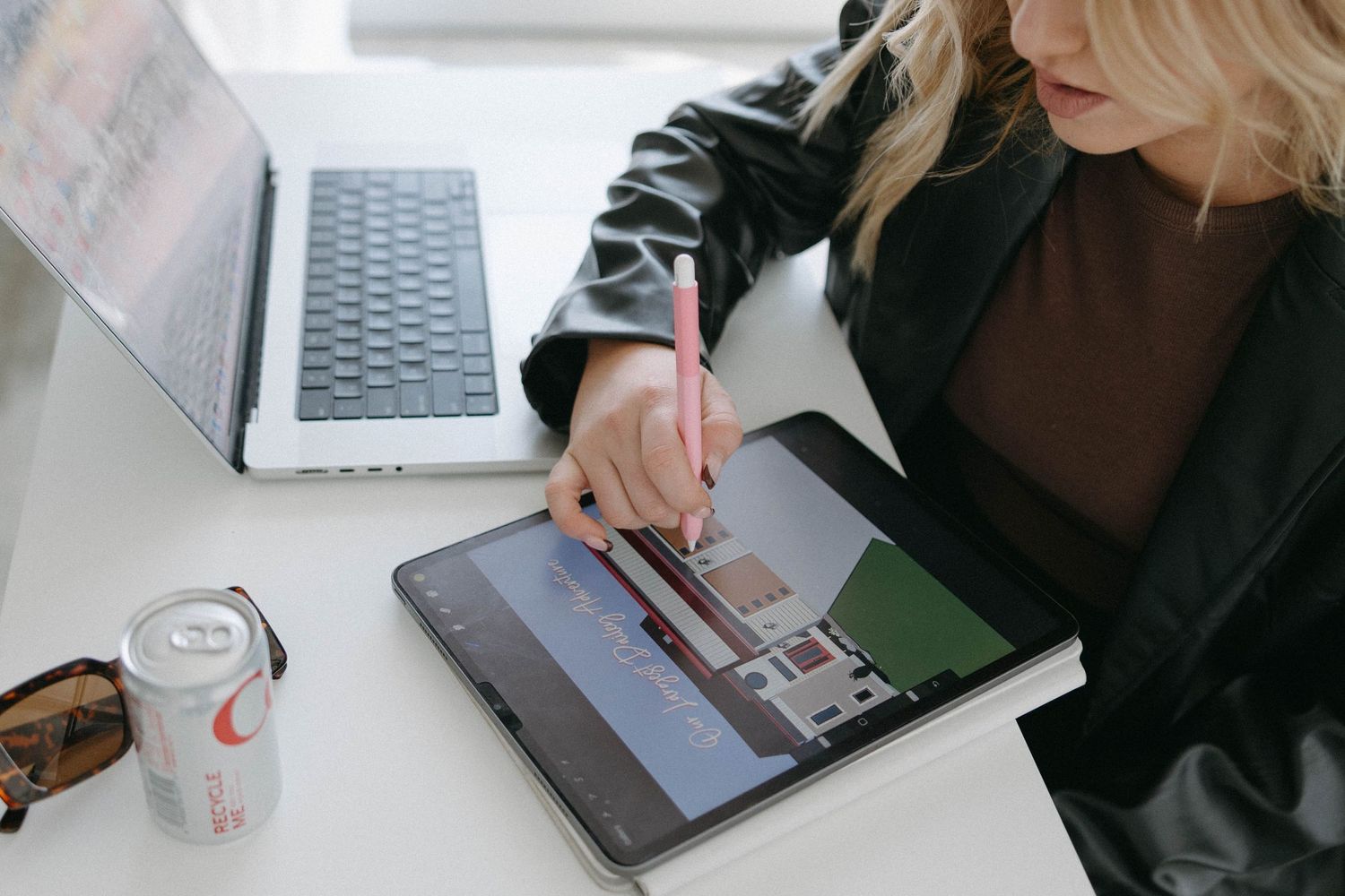 Someone working on a digital tablet with stylus next to laptop and drink.