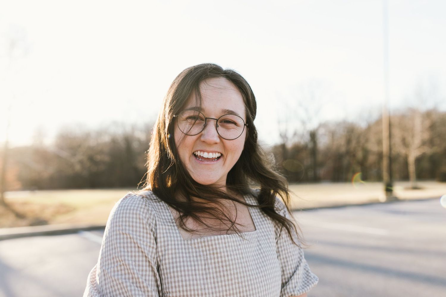 Person with long dark hair and glasses smiling outdoors on a sunny winter day.