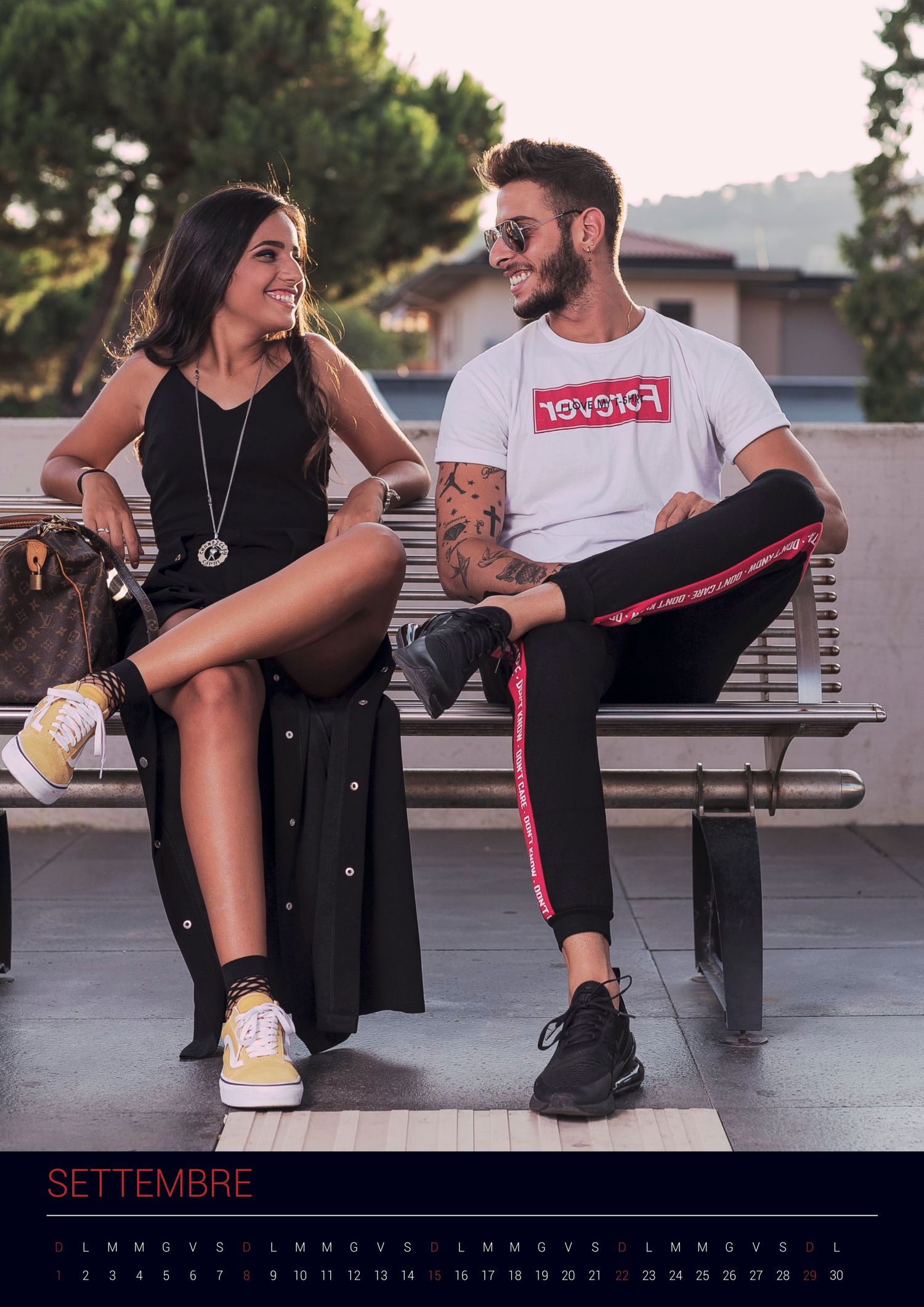A couple sitting casually on a park bench at sunset, wearing trendy streetwear and sneakers.