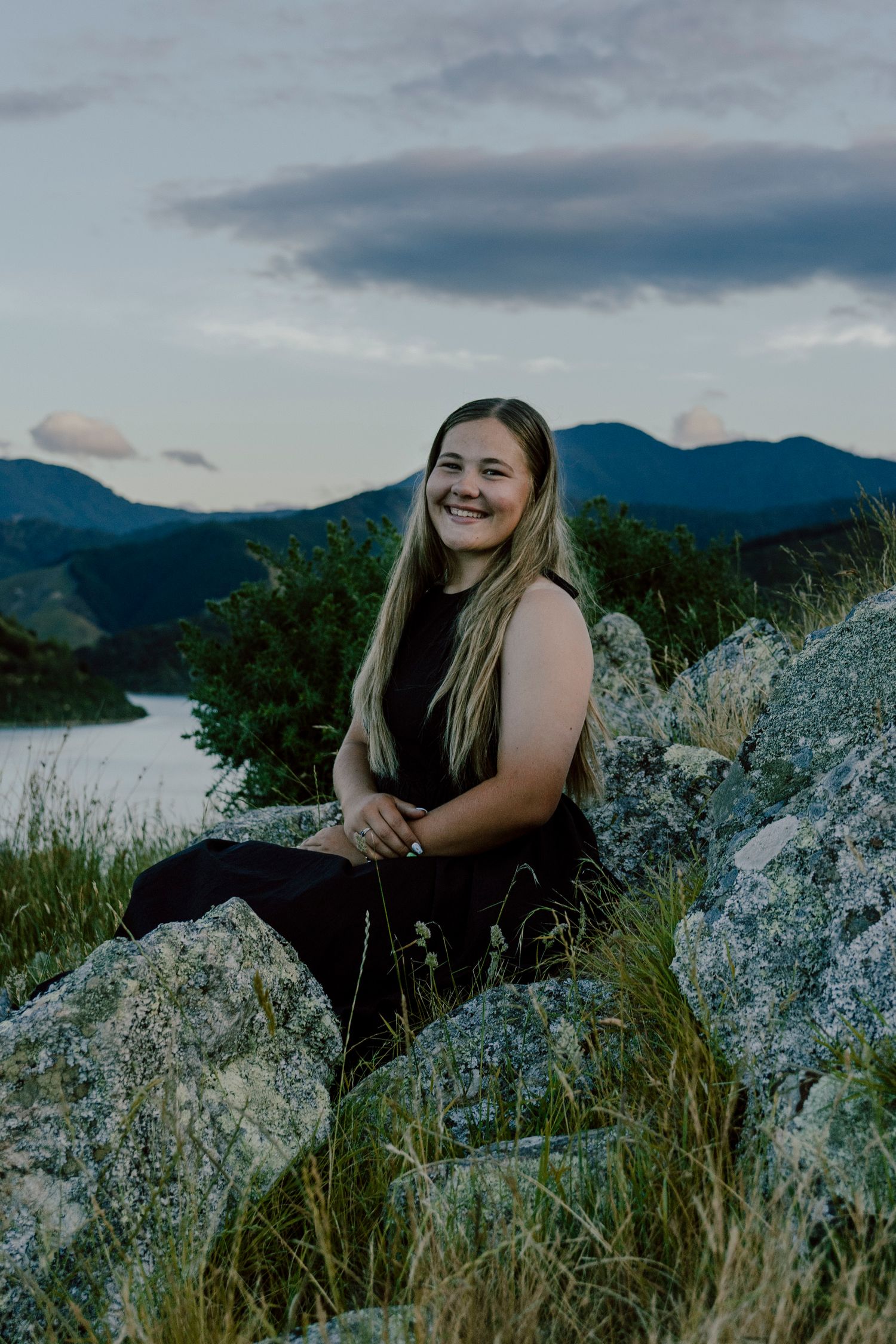 Person sits on rocky outcrop overlooking mountain lake during sunset.