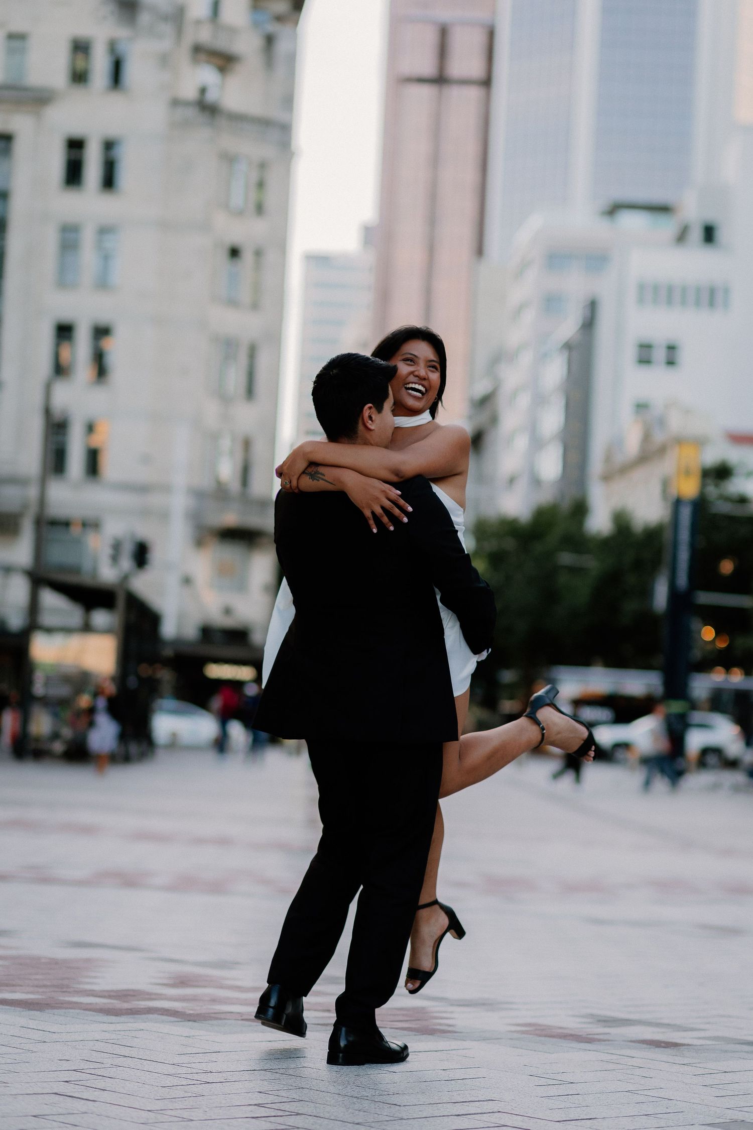 A couple shares a joyful moment together in black and white, laughing while playing in the city centre fountains, Auckland CBD.
