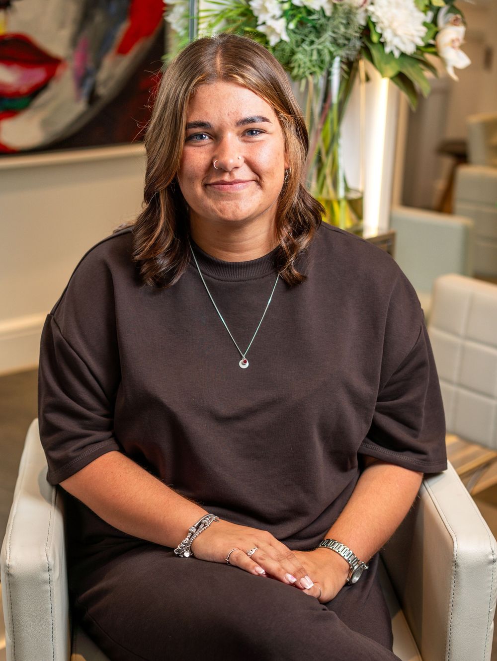 A person wearing a black sweater sits comfortably in a white chair in a well-lit interior setting.