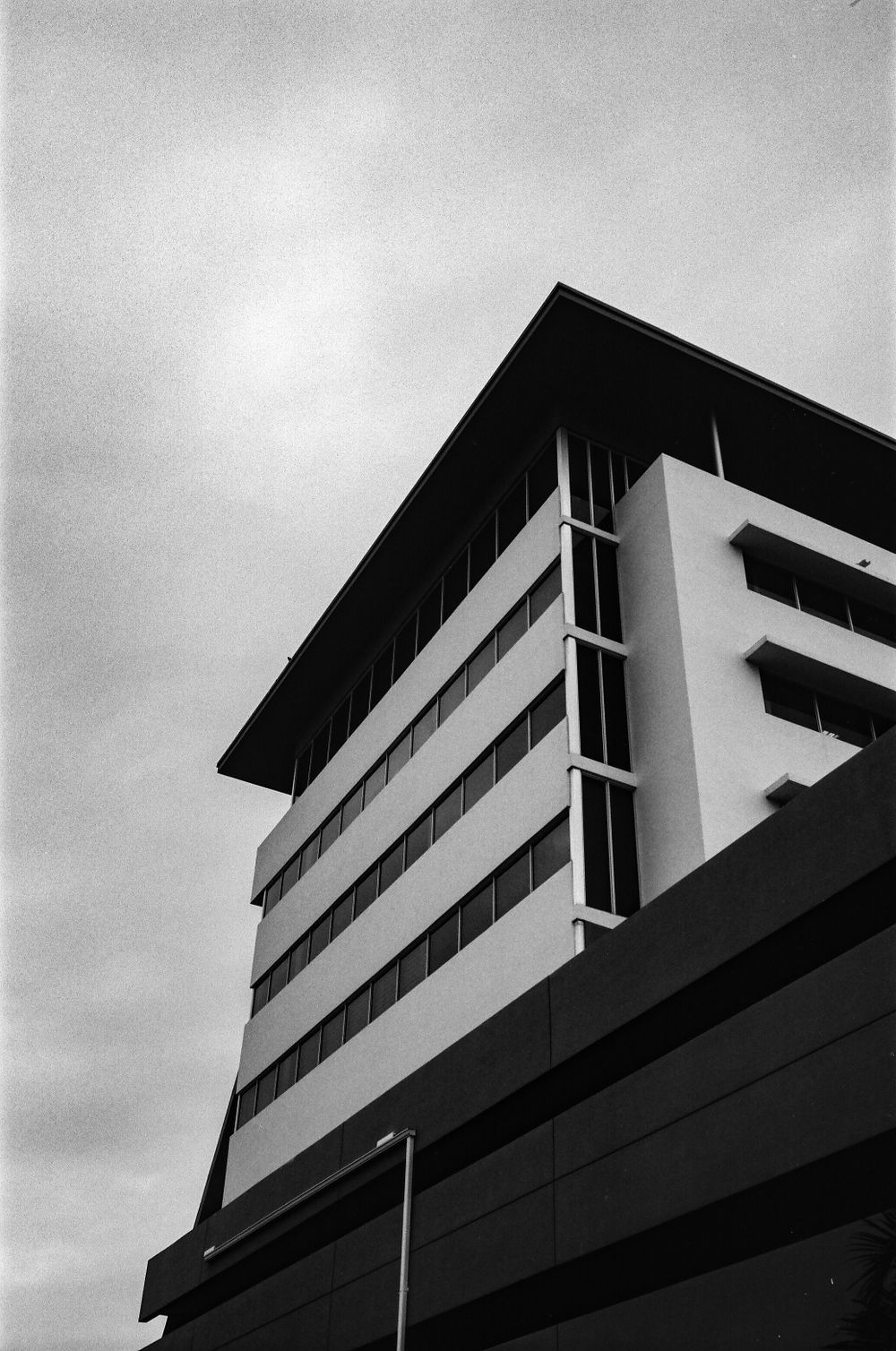 Low angle black and white architectural photo of a modern office building with geometric lines against cloudy sky.