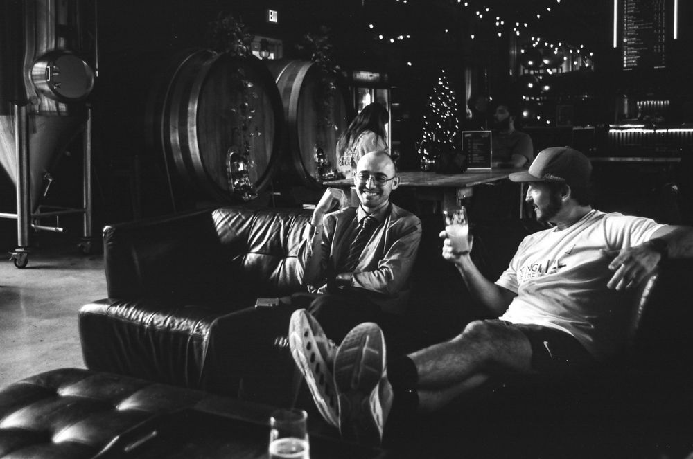 Two people relaxing on leather furniture in a room with wine barrels.