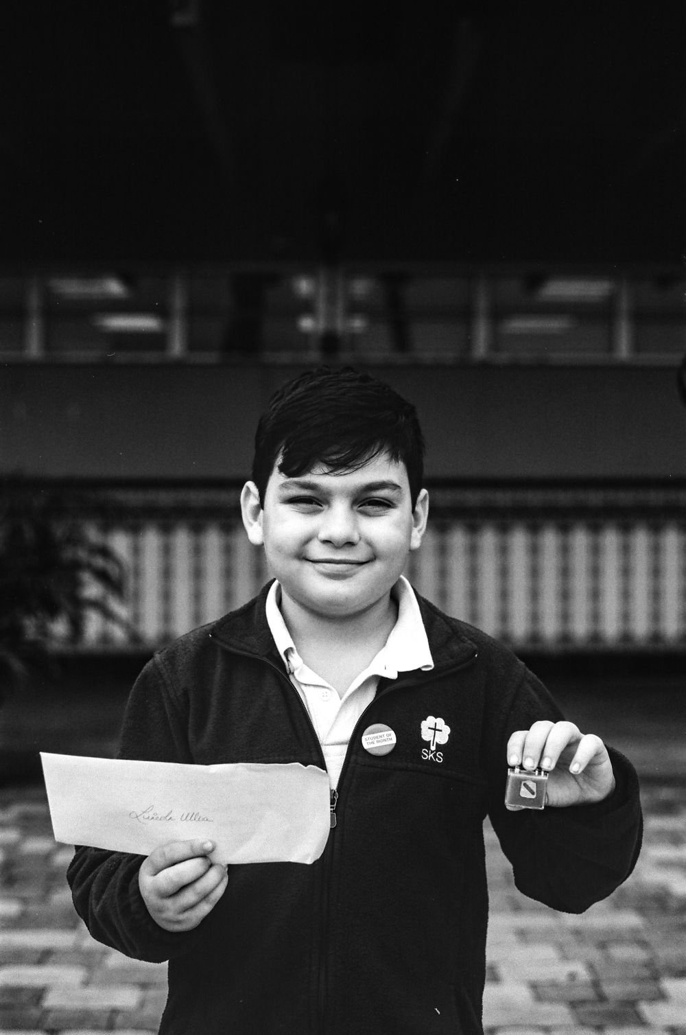 A student holding up an envelope and pin while wearing a school uniform.
