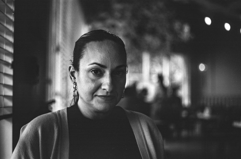 A moody portrait shot through window blinds in black and white.