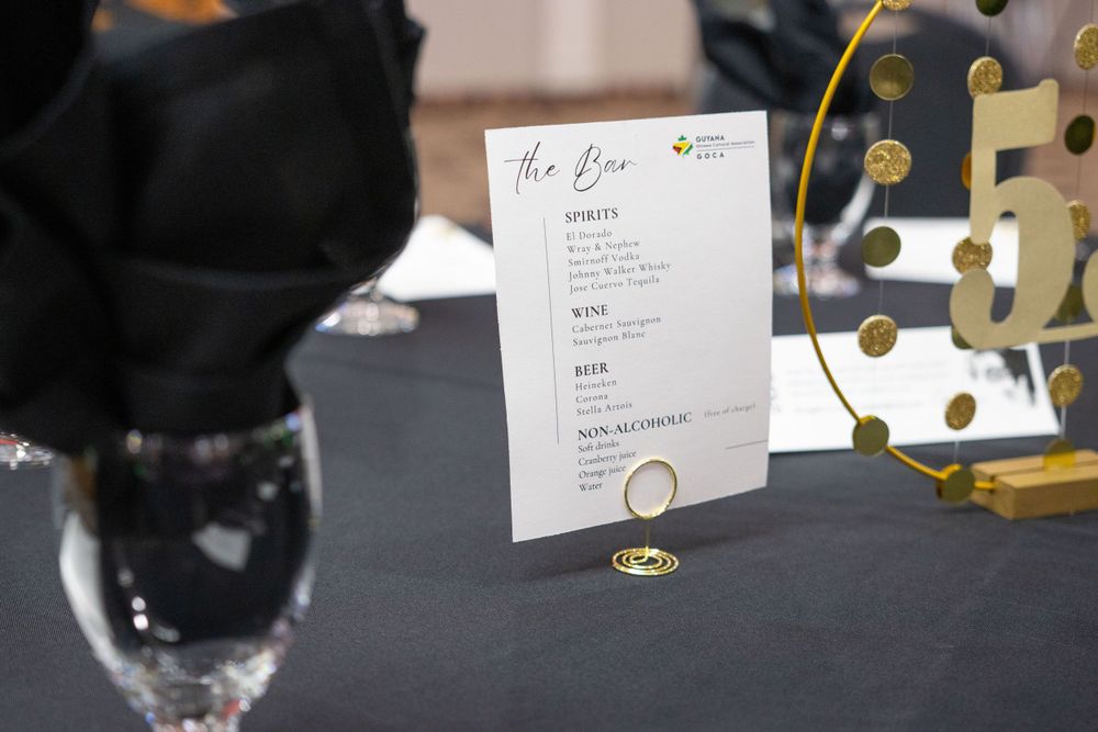 A table setting with a black menu card holder and decorative gold accent pieces on a dark surface.