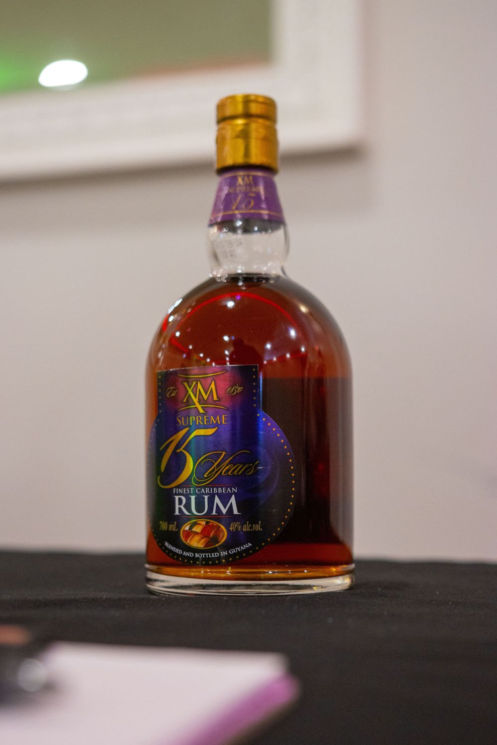 A bottle of XM 5 year aged rum with gold cap and purple label sits on a dark surface.