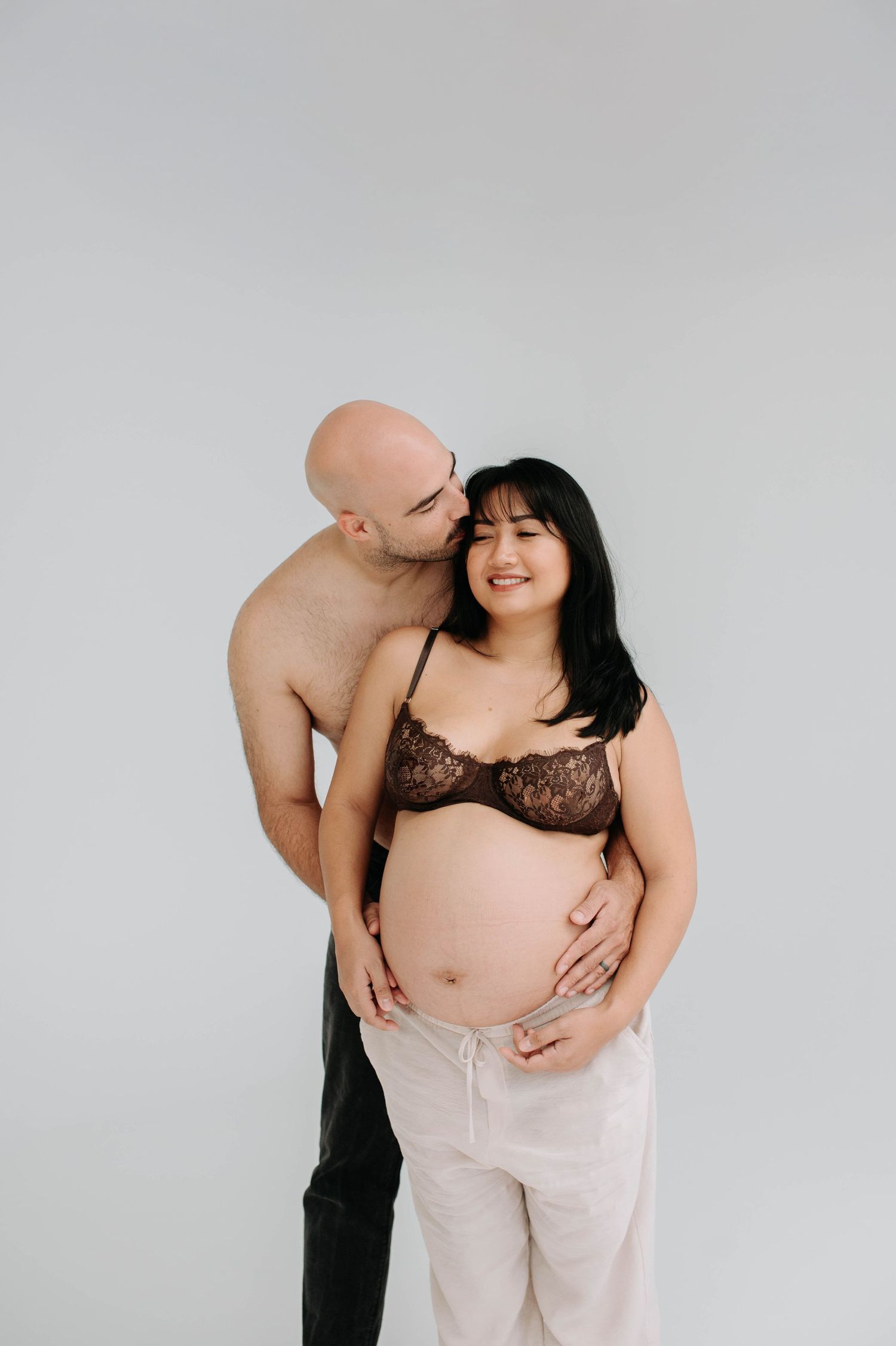Artistic maternity photo of couple sharing intimate moment against white background.