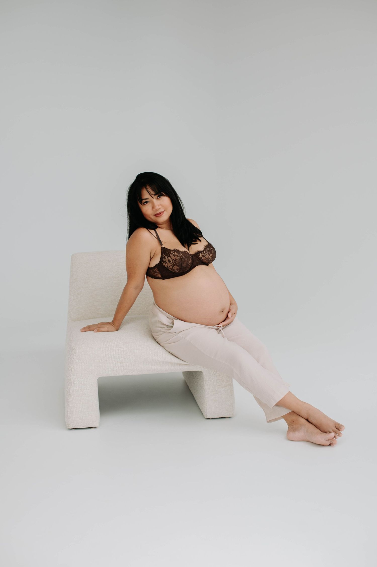 Artistic maternity photo of expecting mother posing on modern white chair.