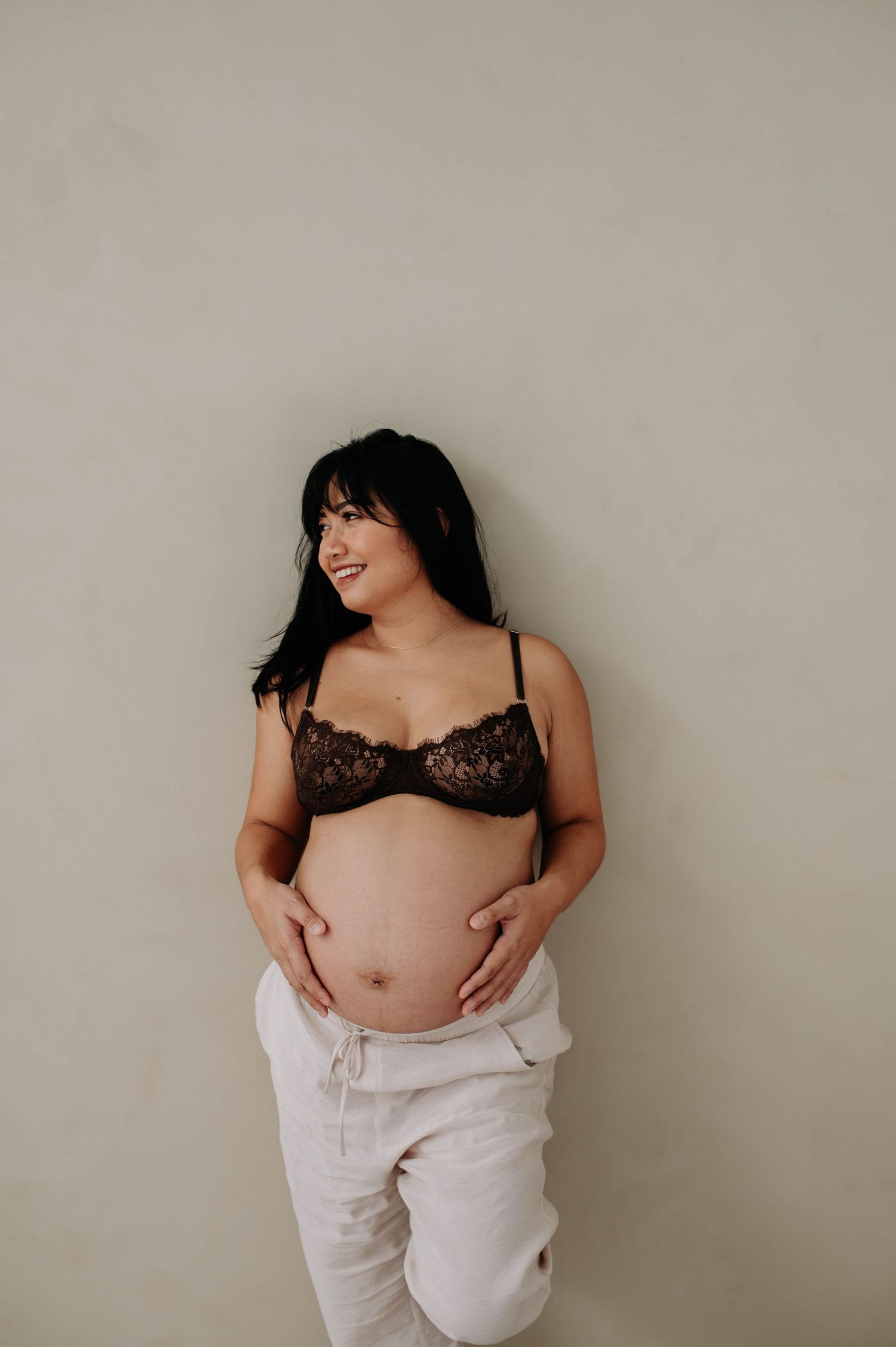 Natural maternity portrait with mother-to-be displaying baby bump against neutral wall.