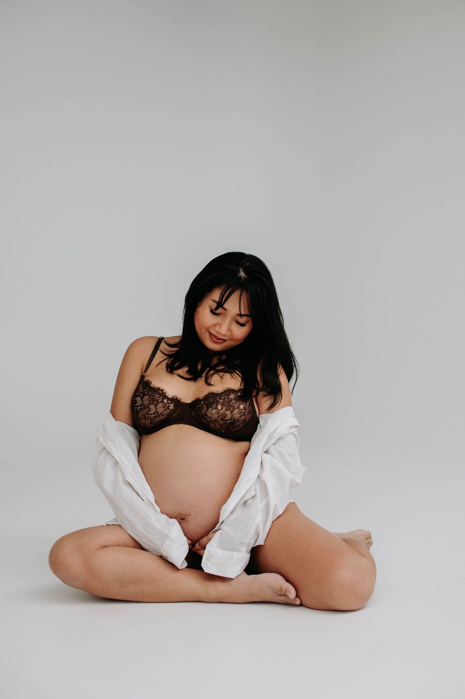 Artistic maternity portrait with expecting mother in white shirt and lace bralette.