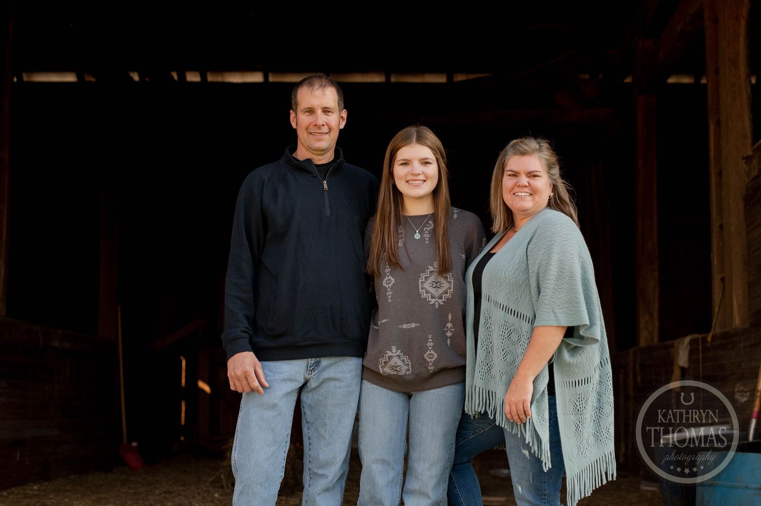 Family portrait of three people standing in rustic barn doorway.