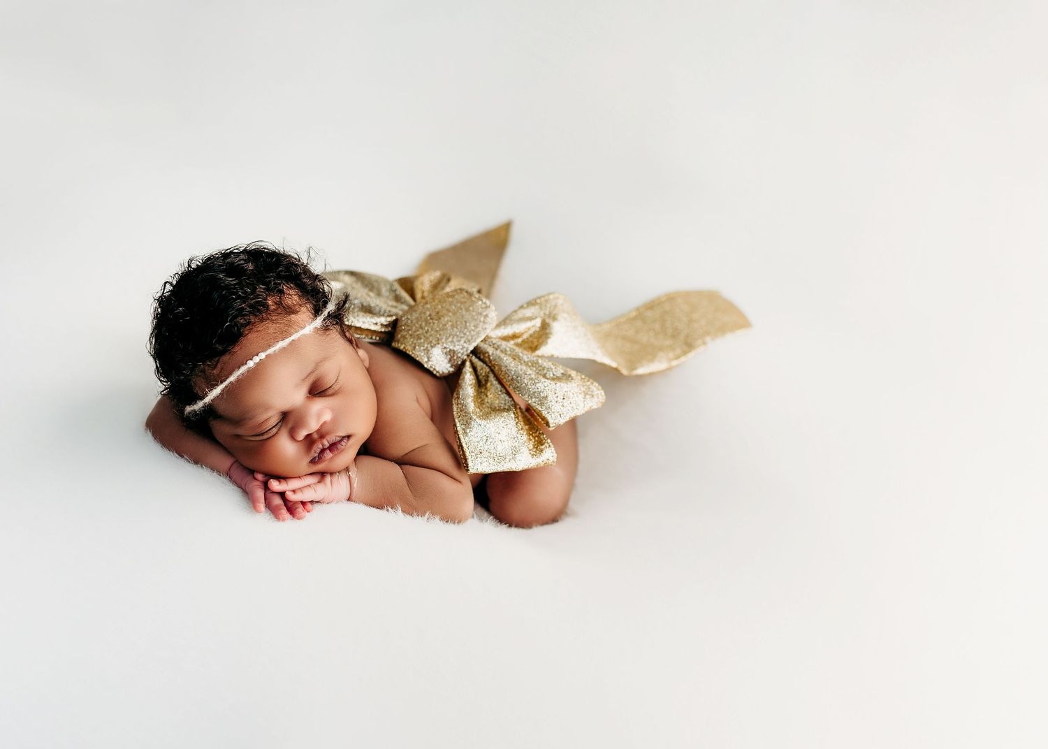 Sleeping newborn wearing gold sparkly angel wings rests peacefully on white backdrop during studio photo session.
