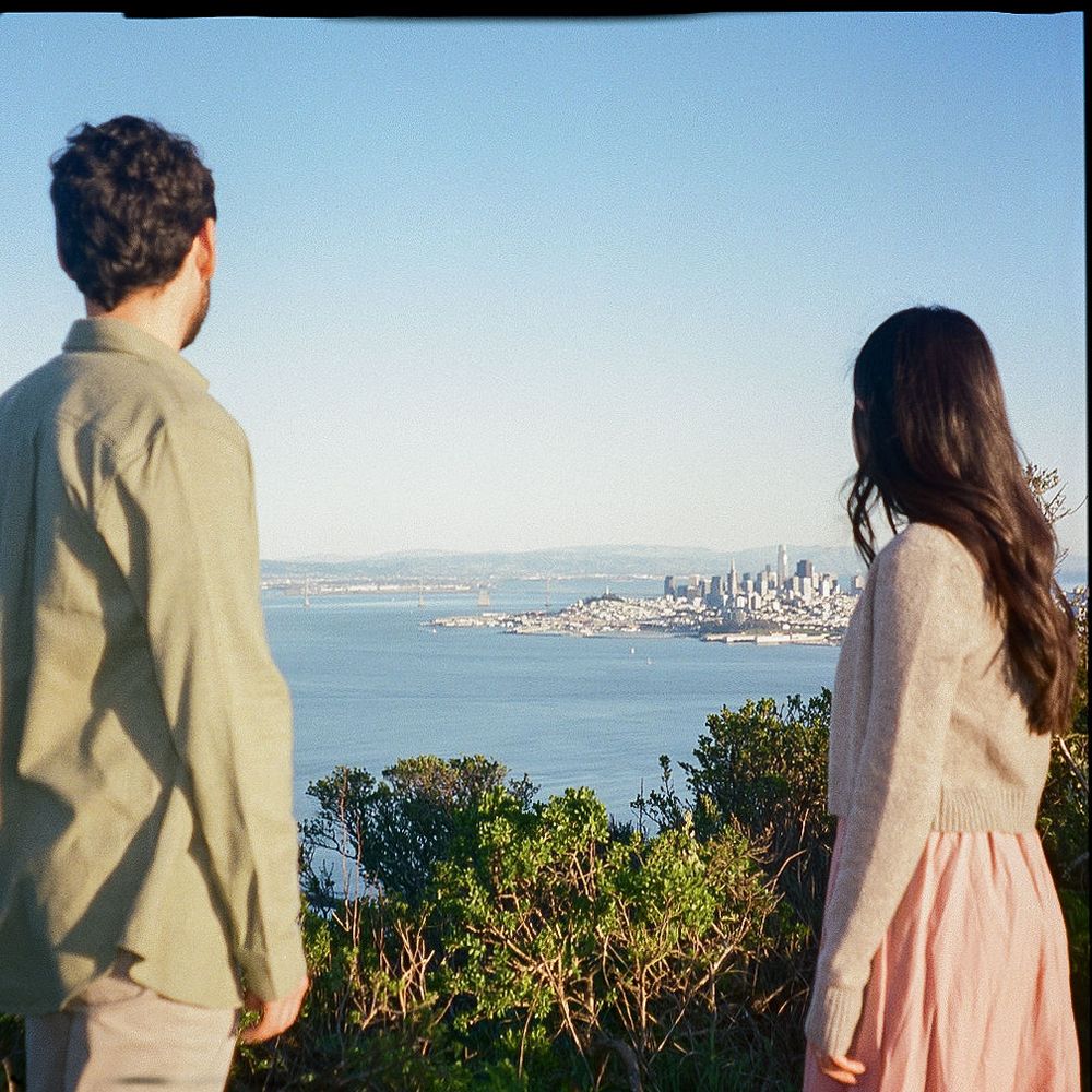 Two people in casual attire admire the San Francisco city skyline and bay view from an elevated vantage point.