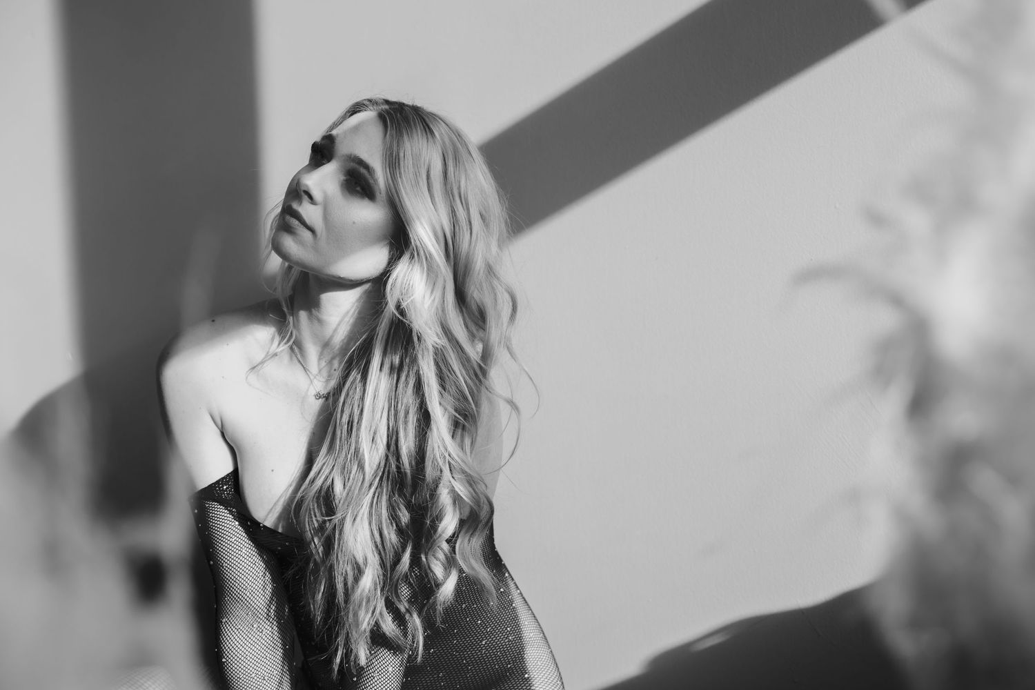 Black and white portrait of someone with long wavy hair in dramatic lighting with shadows on the wall.
