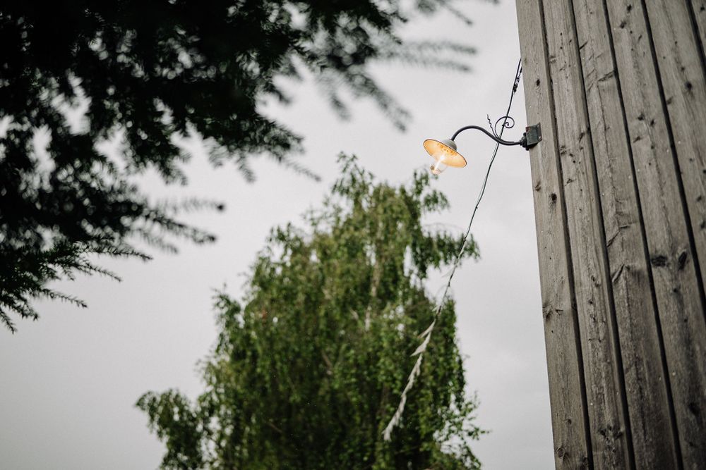 A stick figure light installation mounted between trees and a building glows against an overcast sky.
