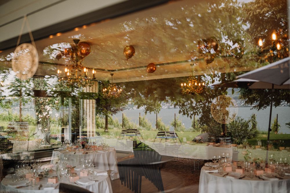 Elegant wedding reception venue with round tables set under sparkling chandeliers and greenery hanging from the ceiling.