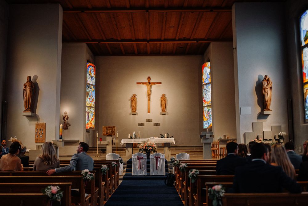 Interior view of a Catholic church with wooden pews, stained glass windows, and a crucifix on the altar during a service.