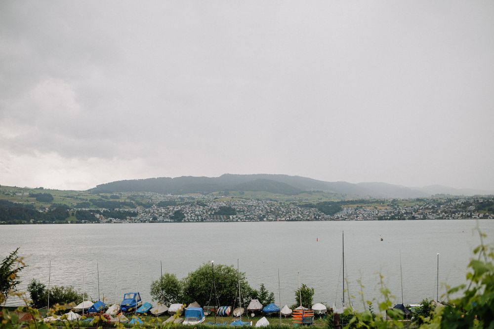 A serene lakeside view with mountains in the background and small boats docked along the cloudy shoreline.