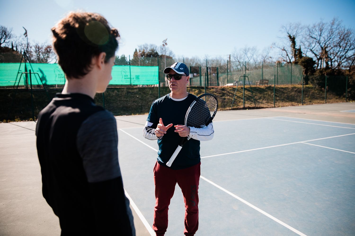 Two people standing on a tennis court having a conversation on a sunny day - Cadart Country Tennis Académie - Aix-en-Provence - France