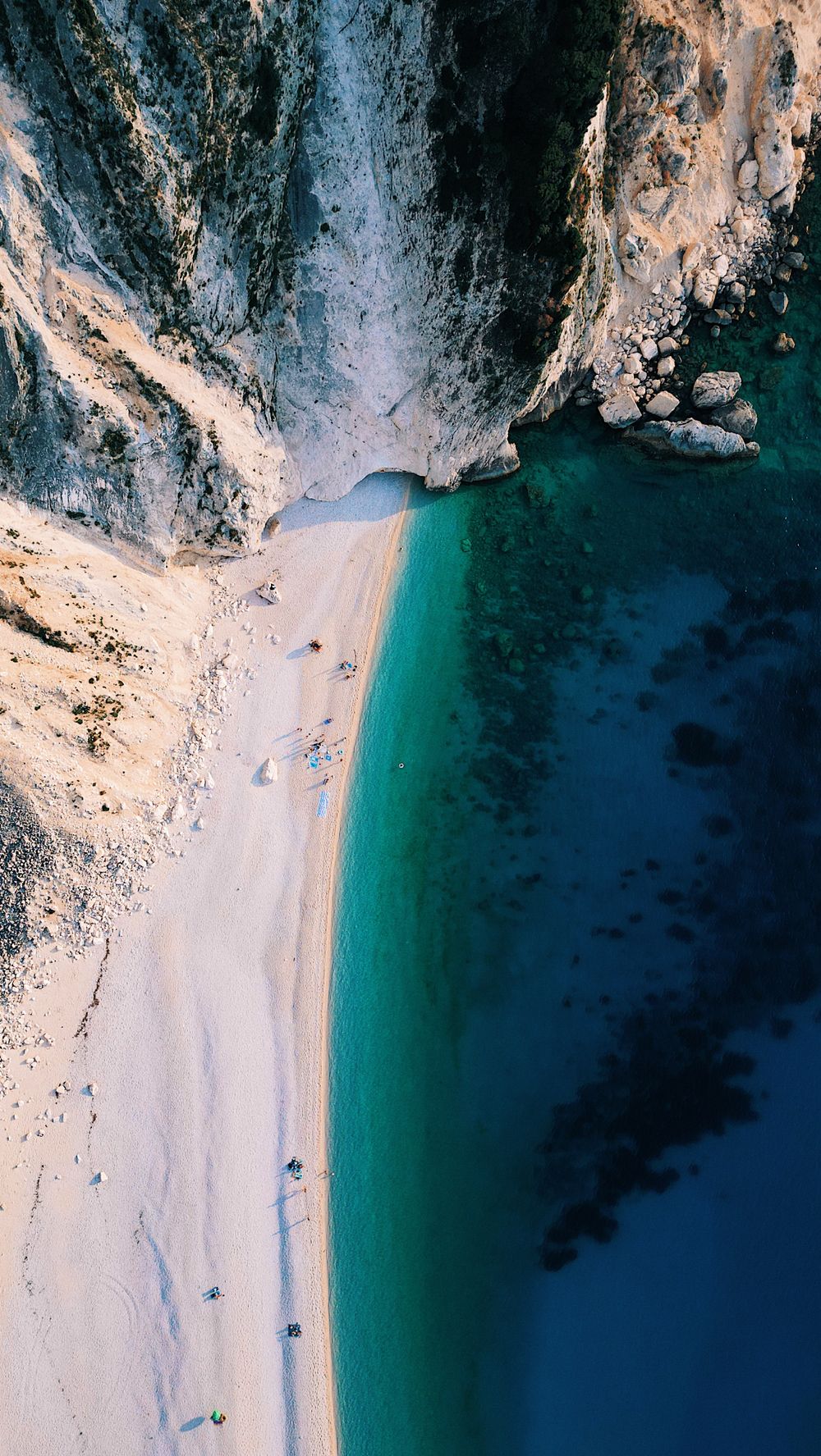 Aerial view of a dramatic coastline with turquoise waters and white sandy beach between steep cliffs.
