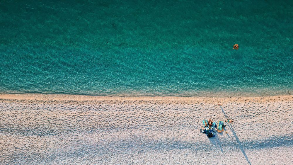 Birds-eye view of a small boat on pristine turquoise waters near a sandy beach.