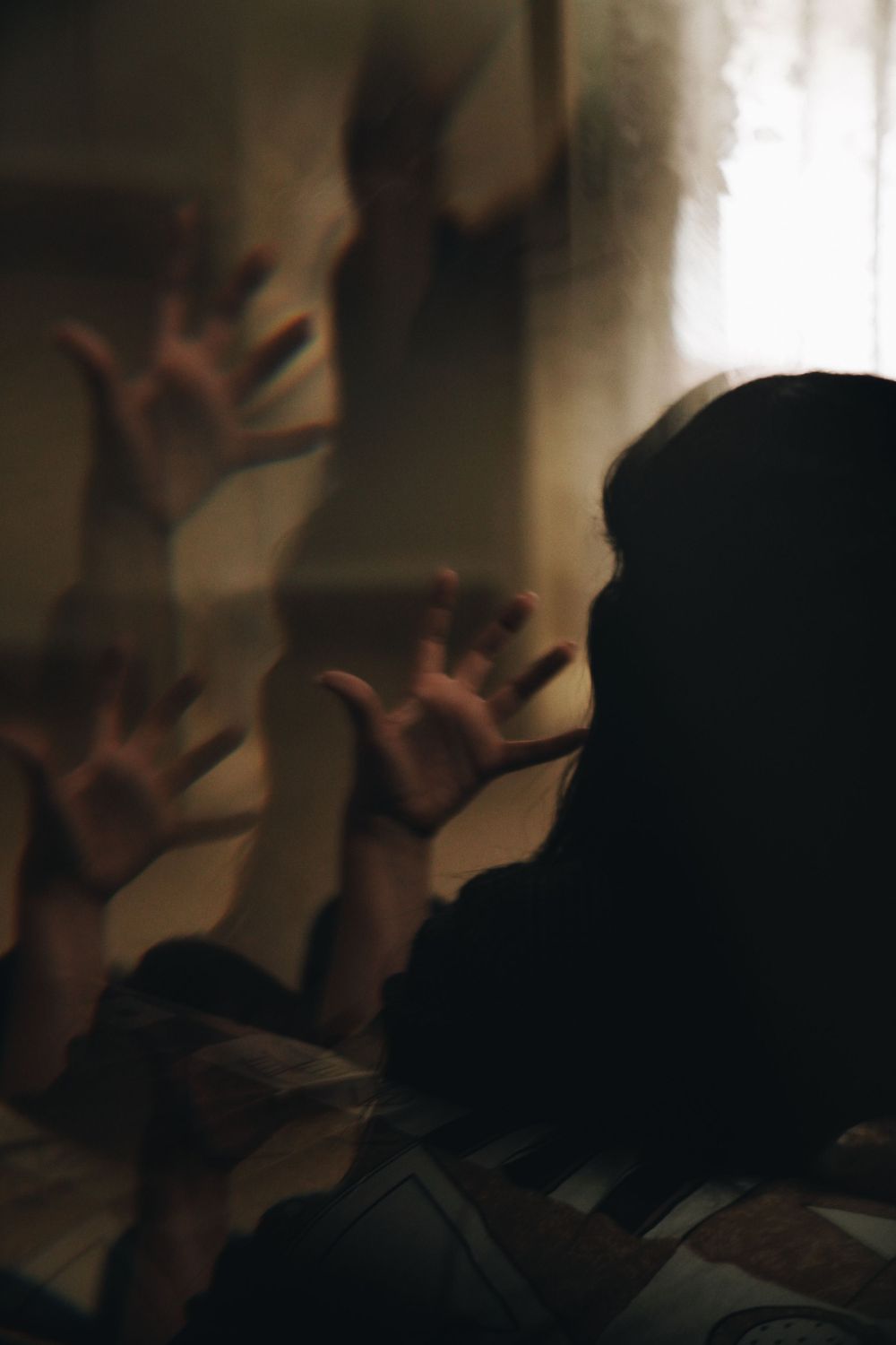 A shadowy silhouette with hands pressed against glass in moody lighting.