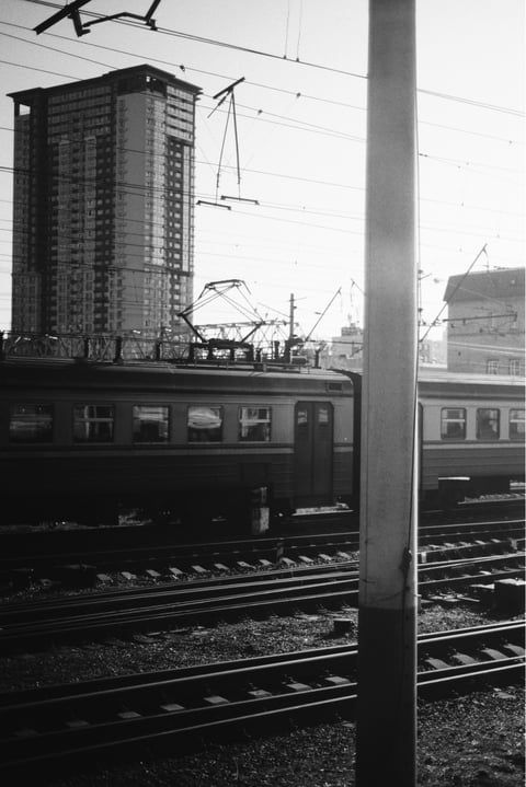 Train cars and electric lines at station with high-rise building in background.