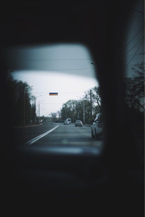View of a street with cars through a car window on a cloudy day with a Russian flag visible.