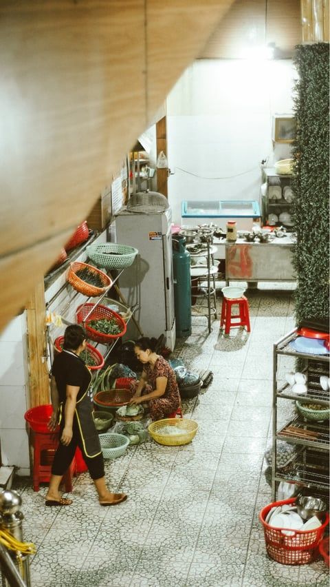 Narrow kitchen workspace with baskets of produce and cooking supplies lined along tiled floor.