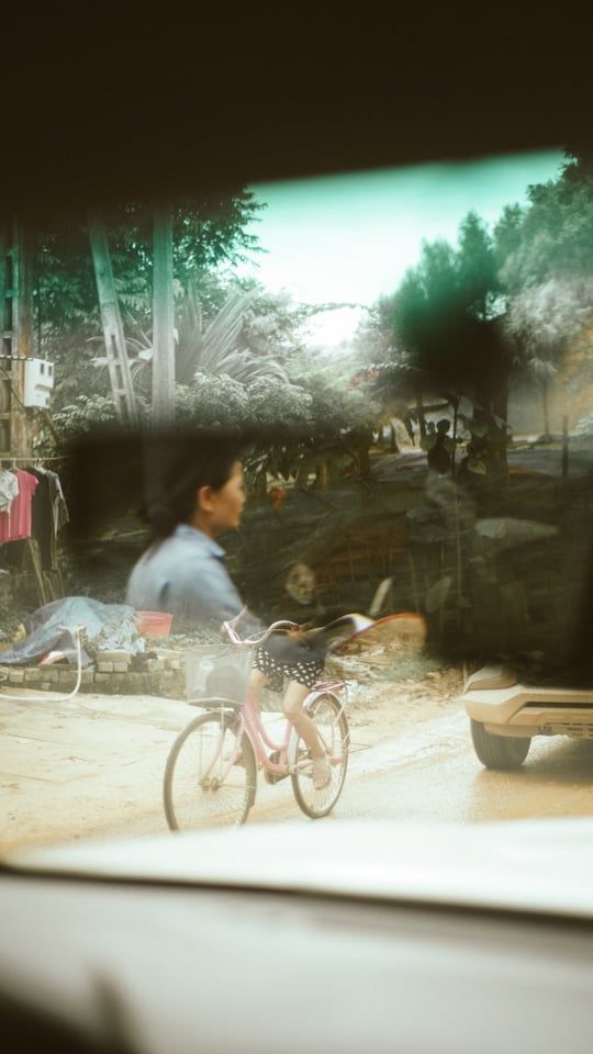 A cyclist riding past on a sunny street viewed through a car window.