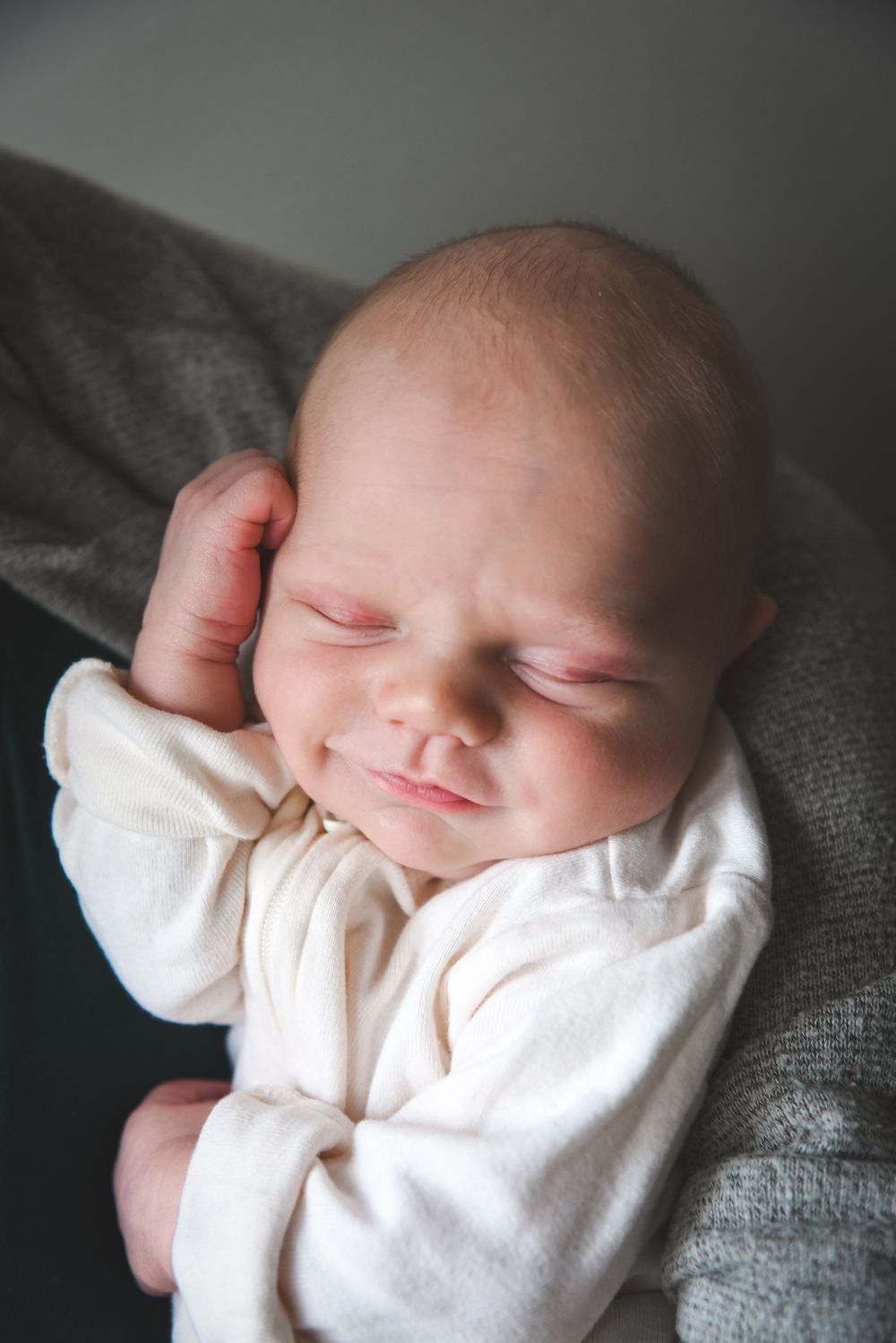 Peaceful sleeping newborn wrapped in soft white fabric against grey textured background.