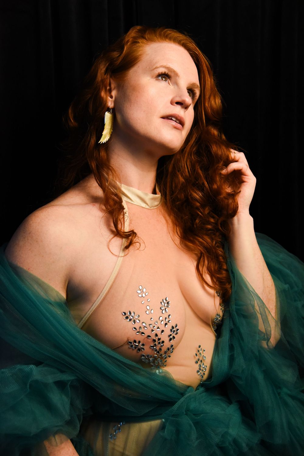 Artistic portrait with teal fabric and decorative body art in dramatic lighting.