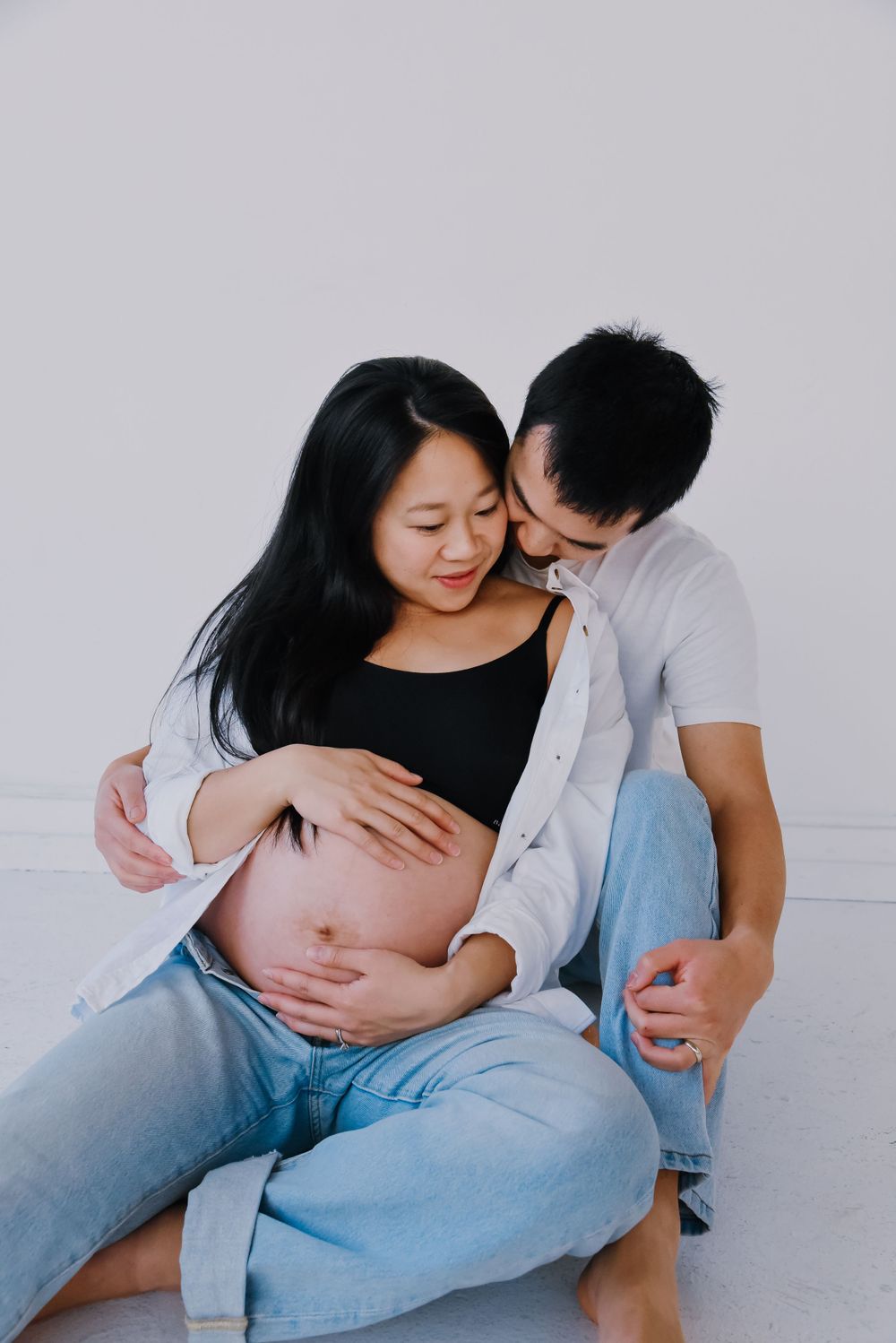 Intimate maternity photo of couple in casual wear against white background.