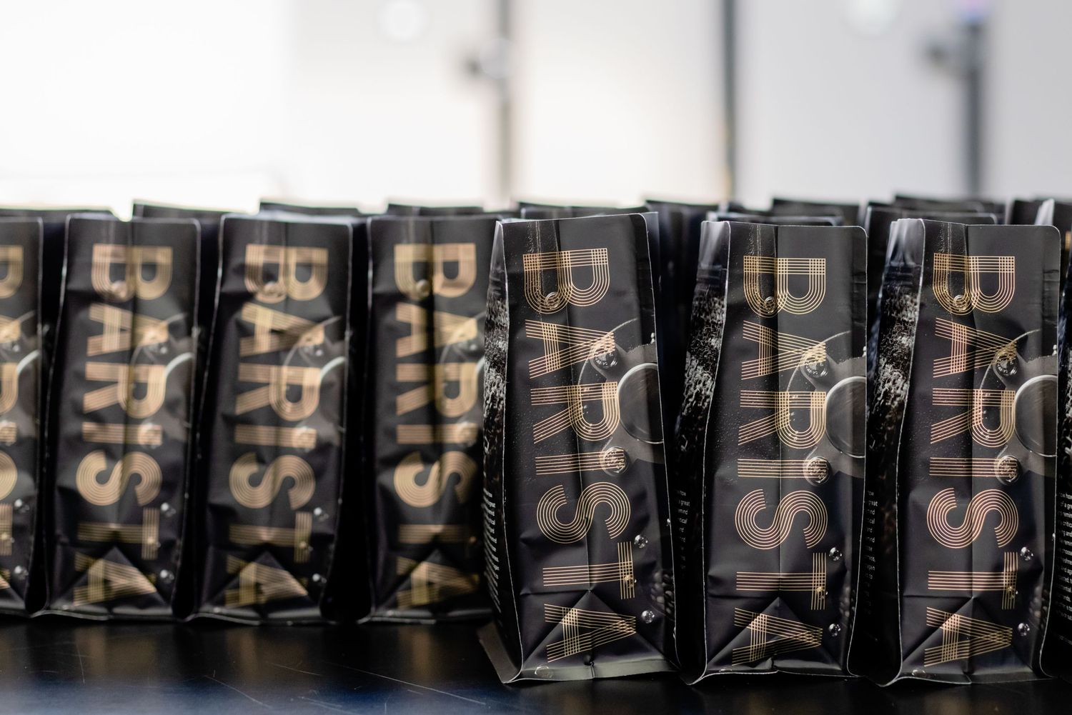 Several coffee bags with gold lettering stand in a row at shallow depth of field.