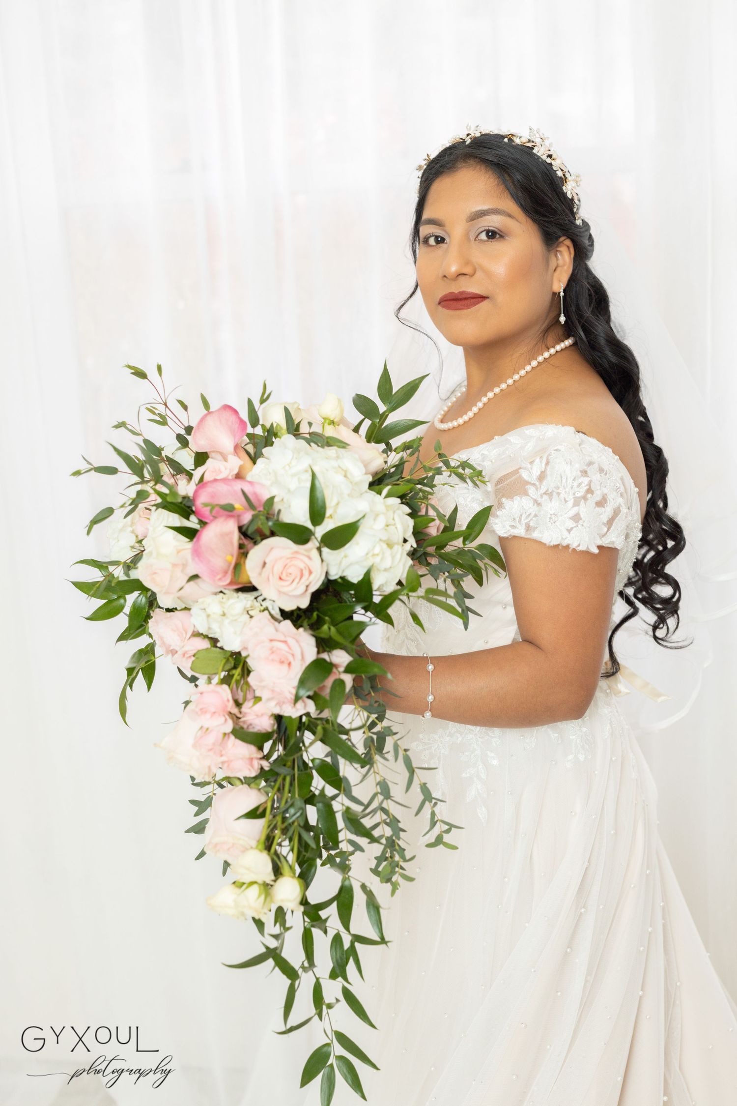 A bridal portrait featuring cascading pink and white bouquet with a lace off-shoulder wedding gown.