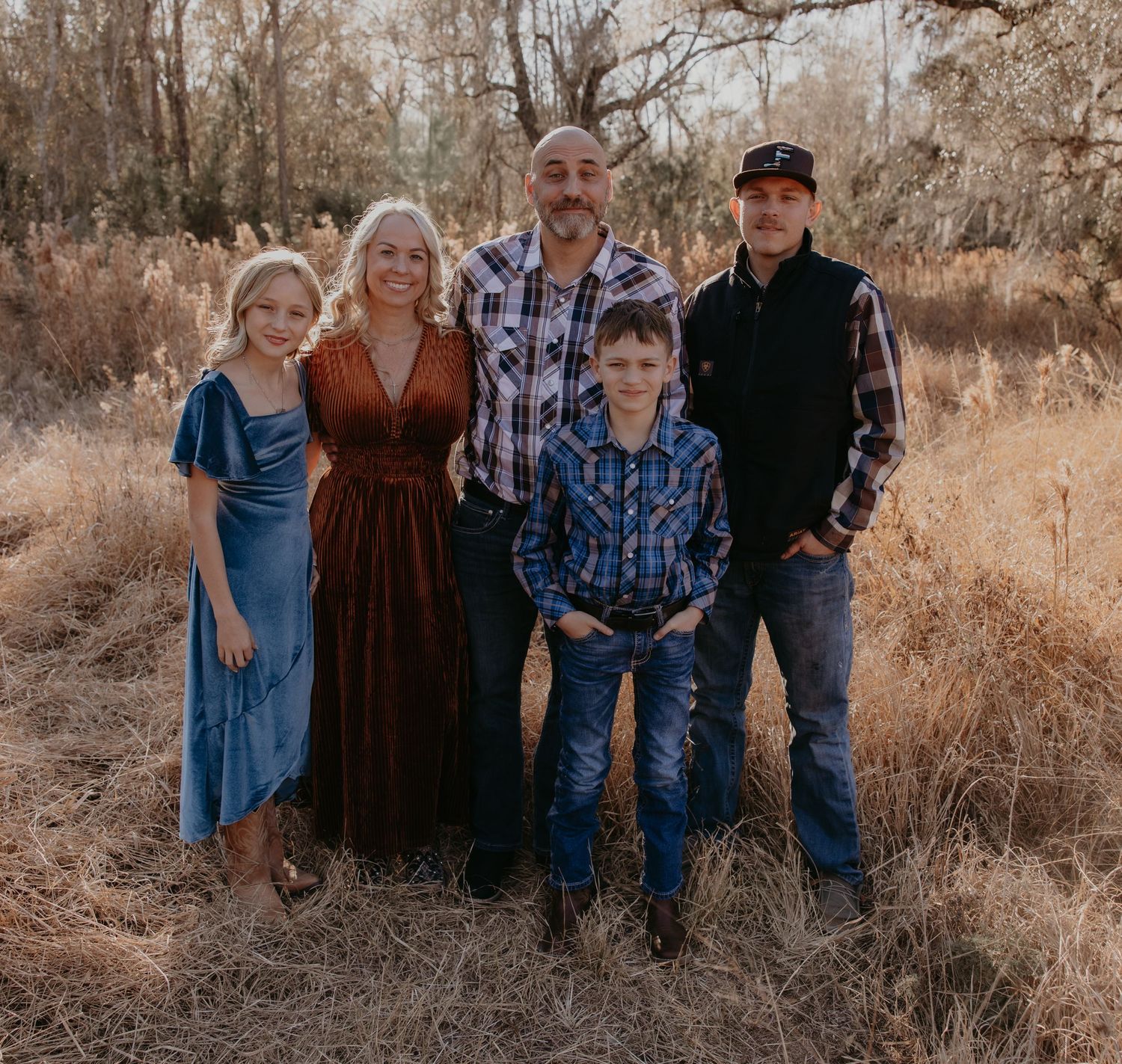 Family of five posing outdoors in a golden field, dressed in coordinated western-style outfits for a fall portrait.