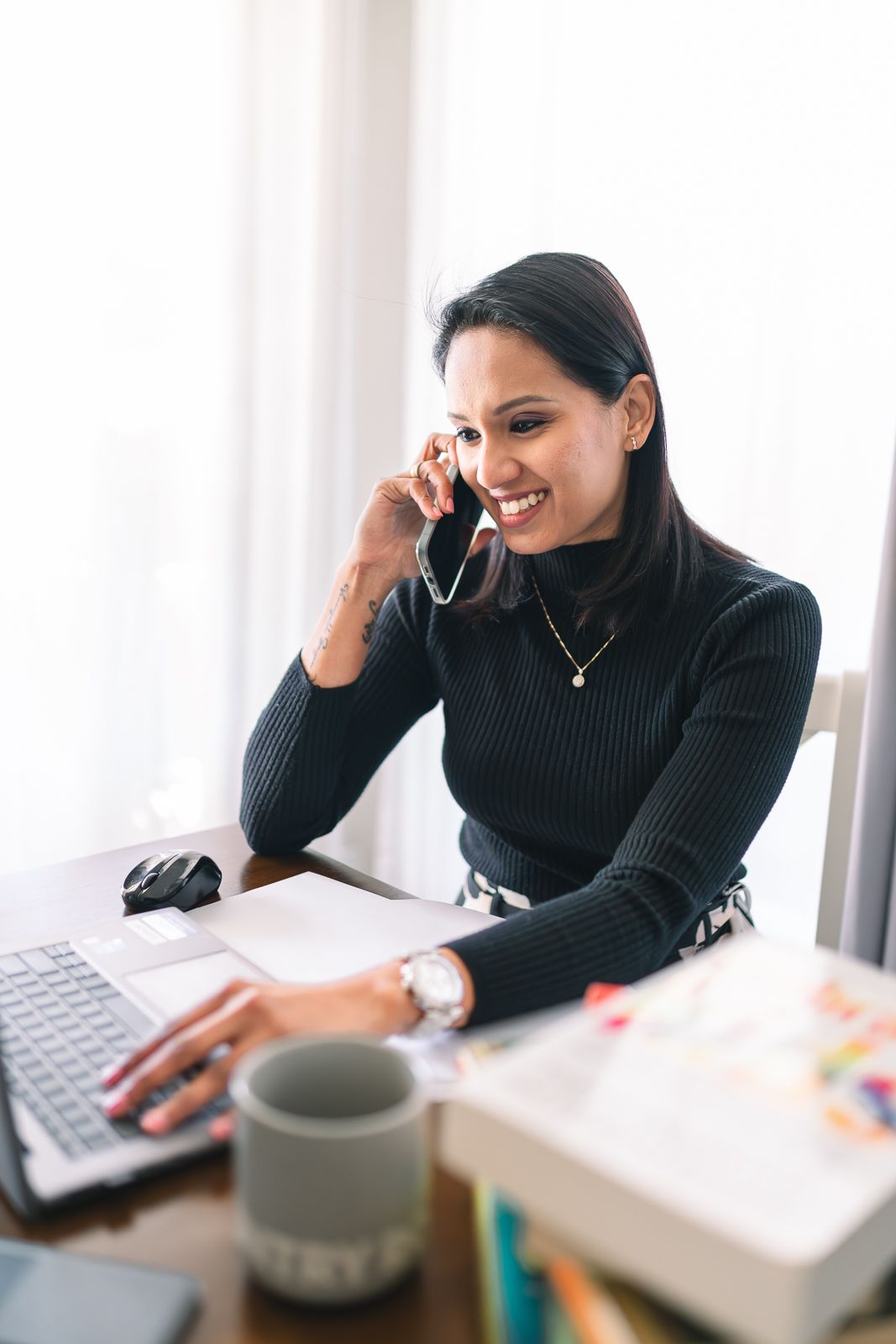 Professional woman in black sweater smiling while working on laptop and talking on phone for a professional branding photoshoot in Melbourne