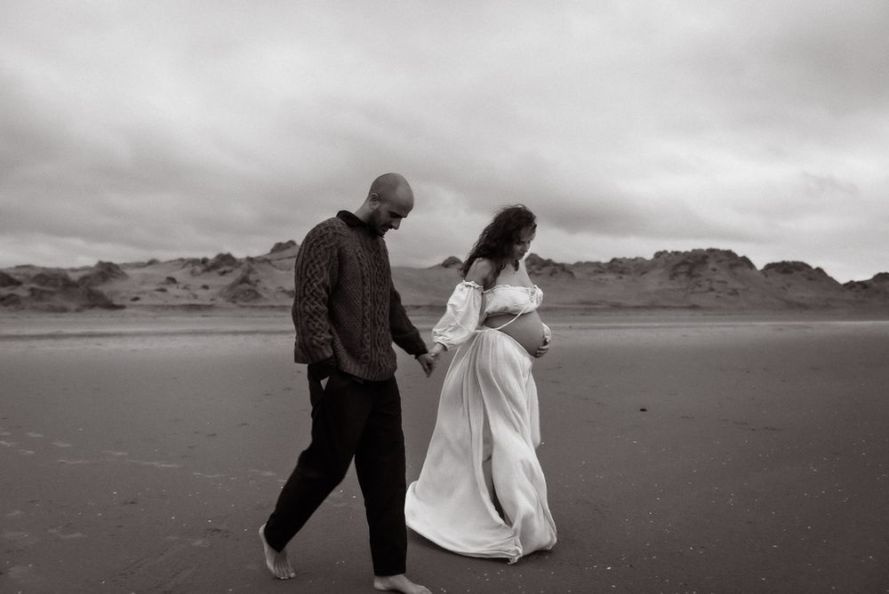 A couple walks hand in hand along a misty beach shore in black and white photography.